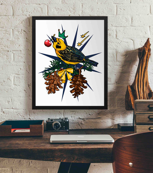 This photo shows the framed Crowned Golden Finch art print hanging on a white brick wall. Below it, there is a wood. The desk has a camera, laptop, and wood sculpture on it.