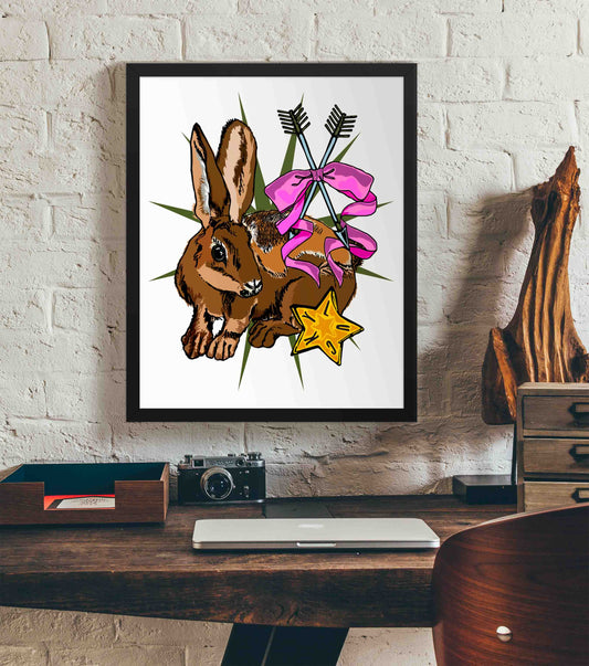 This photo shows the framed Lucky Rabbit's Path art print hanging on a white brick wall. Below it, there is a wood. The desk has a camera, laptop, and wood sculpture on it.