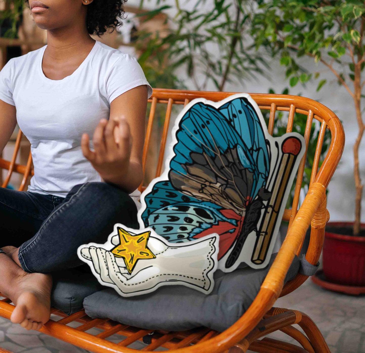 This image shows the butterfly pillow and the Lucky star hand pillow sitting together on a rattan chair next to a woman in a yoga pose.