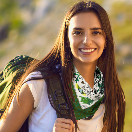 Woman with a green backpack wearing the Mountain Hikes bandana scarf. She's smiling while hiking outdoors.