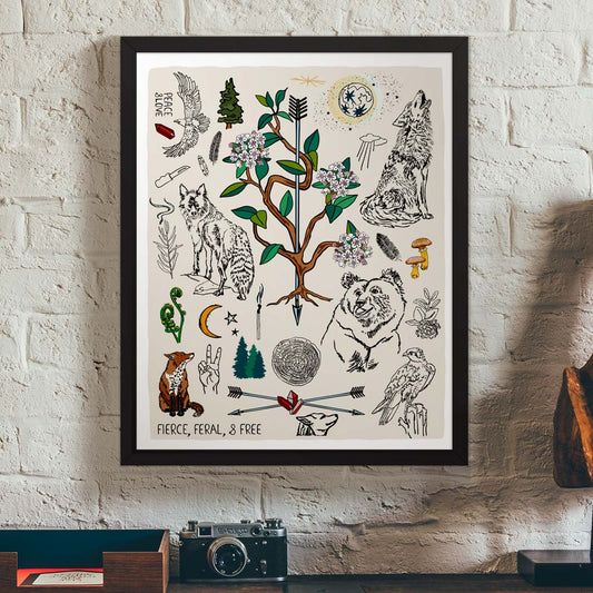 Fierce, Feral, and Free art print poster in a black wood frame hanging on a brick wall, above a vintage desk.