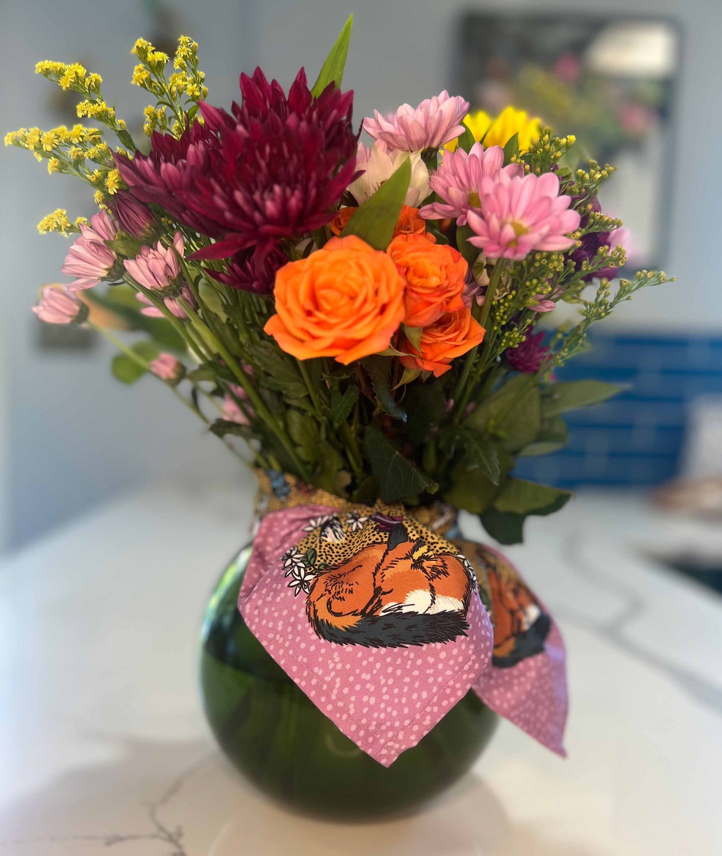 Fox bandnan tied around a green glass vase of flowers.