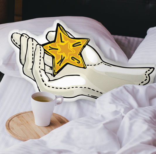 This photograph shows the glove and star-shaped pillow nestled in the white covers of a bed. There is a black headboard and a wooden tray with a coffee mug on the bed.