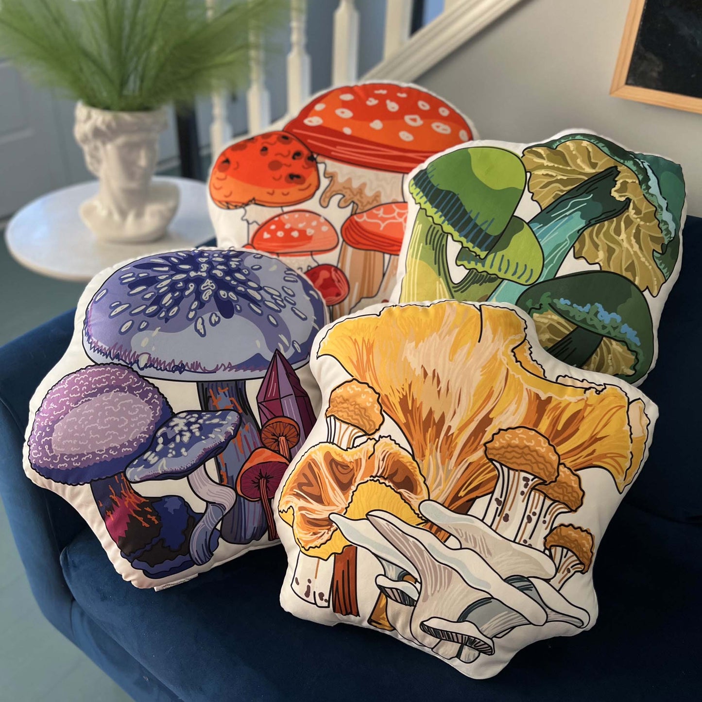 This is a photo of all the mushroom pillows in the collection. They are sitting on a blue couch. There are four color variants; red, green, purple, and yellow.
