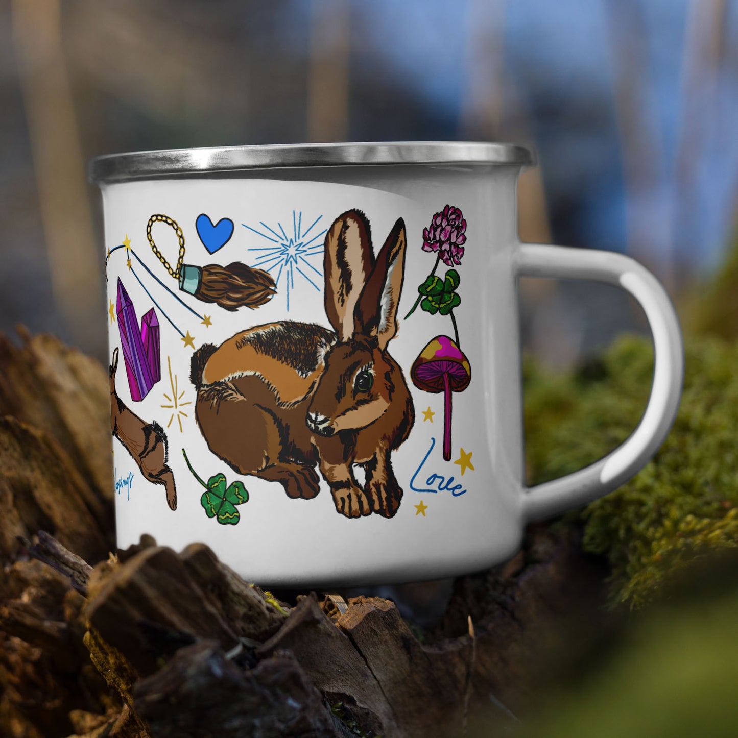 The Orion Stars Camp Mug sitting on a tree stump in the woods. The base color of the enamel cup is white and the artwork is hand drawn illustrations of the Orion constellation, which holds the "Three Lucky Stars", long considered to symbolize prosperity, longevity, and happiness. The art includes lucky rabbits, four-leaf clovers, mushrooms, stars, matches, bows and arrows for loyalty, and other symbols of good fortune. The color palette is golden yellows, pinks, forest greens, and vibrant blues.