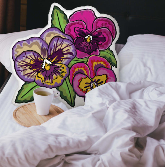 Pansy-shaped pillow nestled in an unmade bed. There is a cup of coffee sitting on a wooden tray.