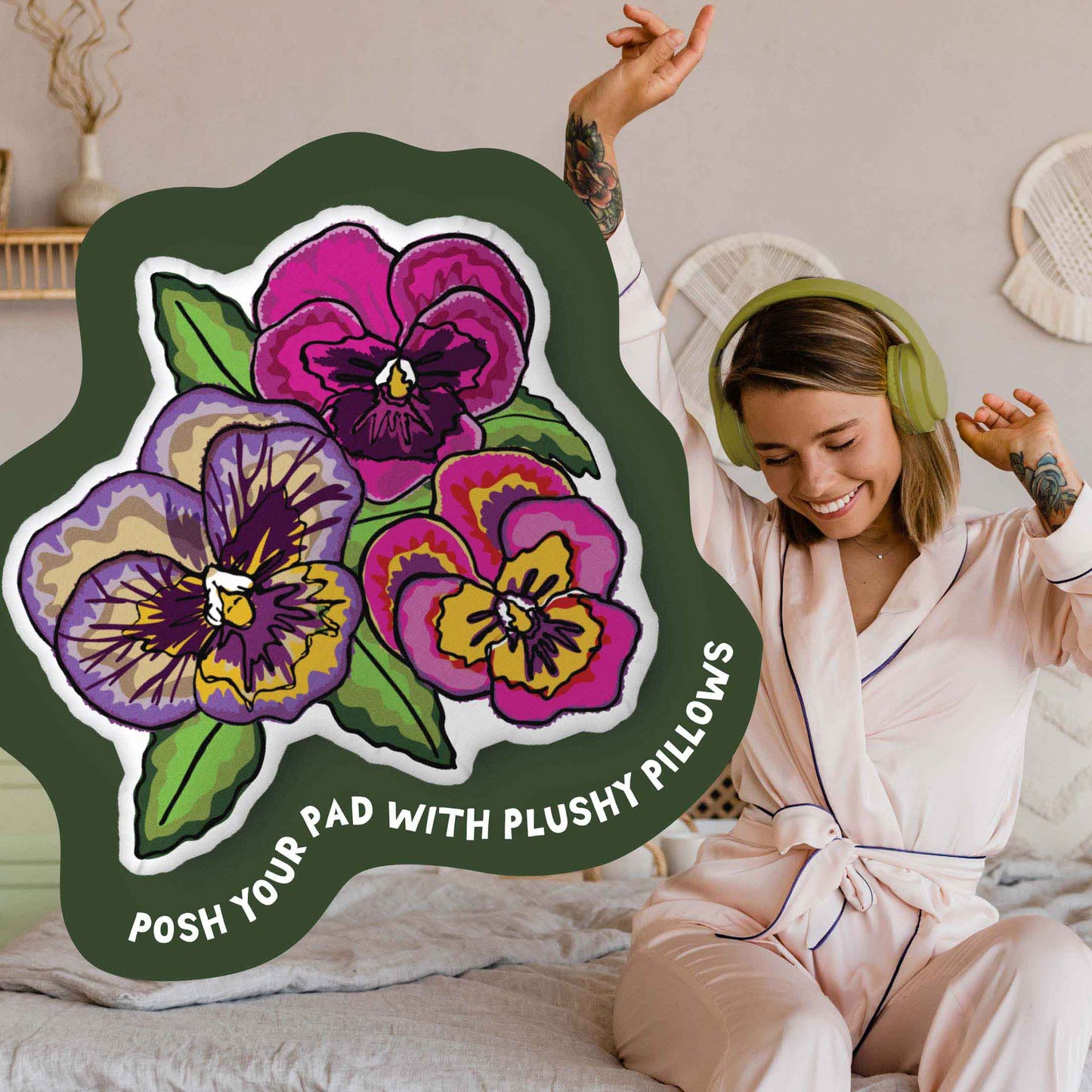 This image shows a photo of the pansy-shaped pillow in a green organic shape. Inside the shape are the words "Posh your pad with plushy pillows". In the background, there is a photo of a woman in pajamas wearing headphones and sitting on a bed.