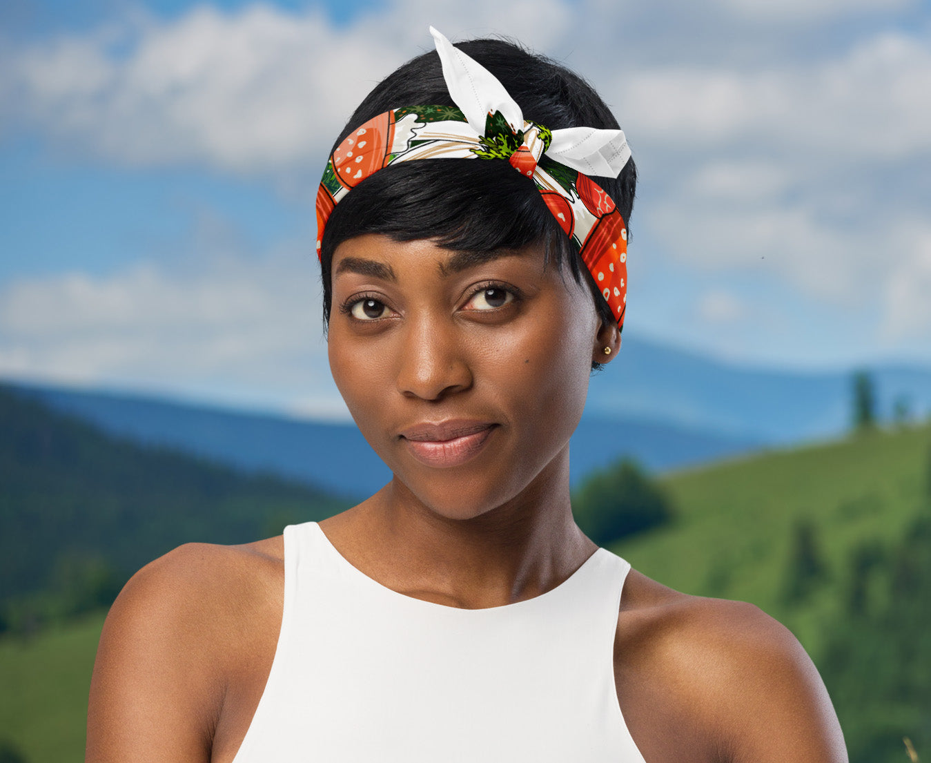 This is an image of a woman wearing the red mushroom scarf tied around her head as a headband standing in front of a mountain range.