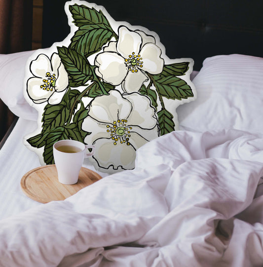 Rose-shaped pillow nestled in an unmade bed. There is a cup of coffee sitting on a wooden tray.