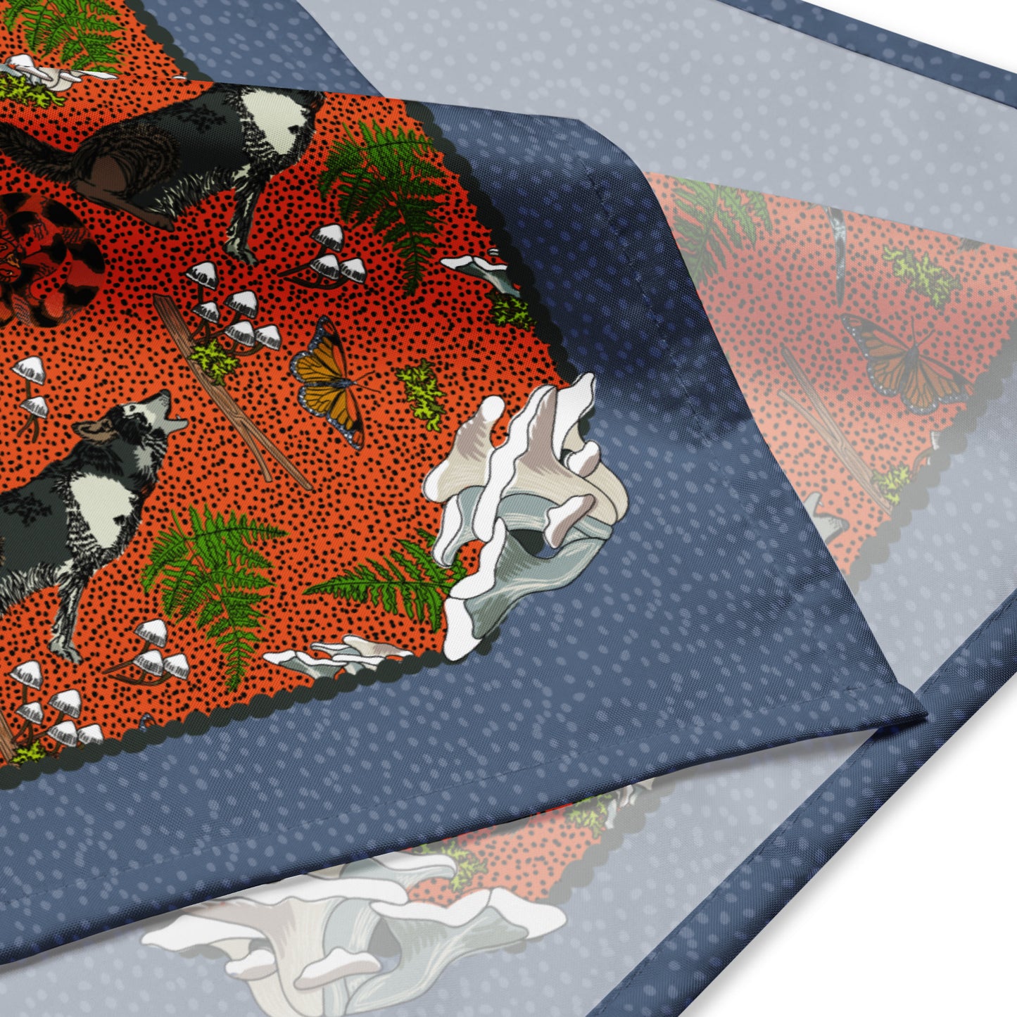 Close up detail of the bandana scarf. It shows the illustrated pattern of wolves, mushrooms, butterflies, moss, and ferns.