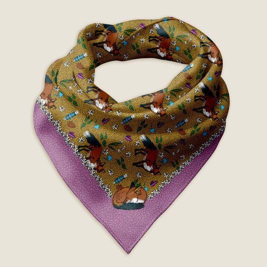 Fox bandana on an ivory background. The pattern around the outside is purple with hand drawn dots and a row of white flowers. The middle pattern has a yellow background with illustrations of foxes, feathers, crystals, pinecones, leaves, and mushrooms.