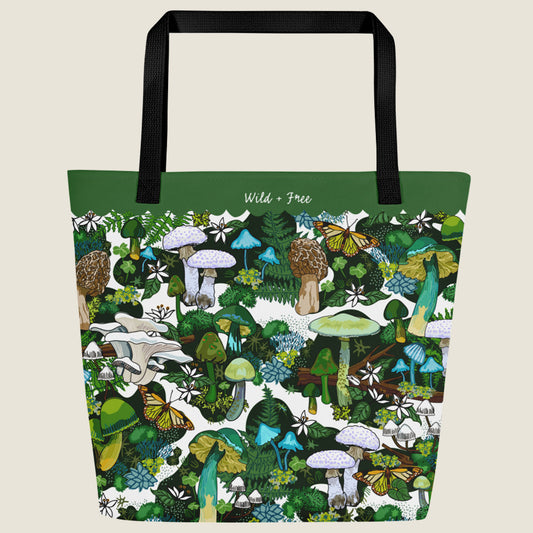 Purple mushroom-themed oversize tote with large interior pocket. This design has green, blue, white, and brown mushrooms, moss, ferns, white flowers, butterflies, and four-leaf clovers. The words "Wild + Free" are written in the green border at the top.