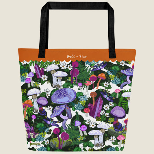 Purple mushroom-themed oversize tote with large interior pocket. This design has purple, pink, white, and orange mushrooms, moss, ferns, white flowers, dragonflies, and crystals. The words "Wild + Free" are written in the orange border at the top.