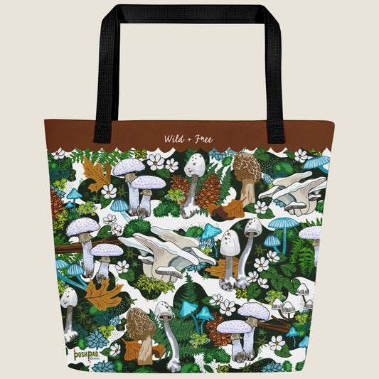 White mushroom-themed oversize tote with large interior pocket. This design has white, blue, and brown mushrooms, moss, ferns, white flowers, fall leaves, and pinecones. The words "Wild + Free" are written in the brown border at the top.