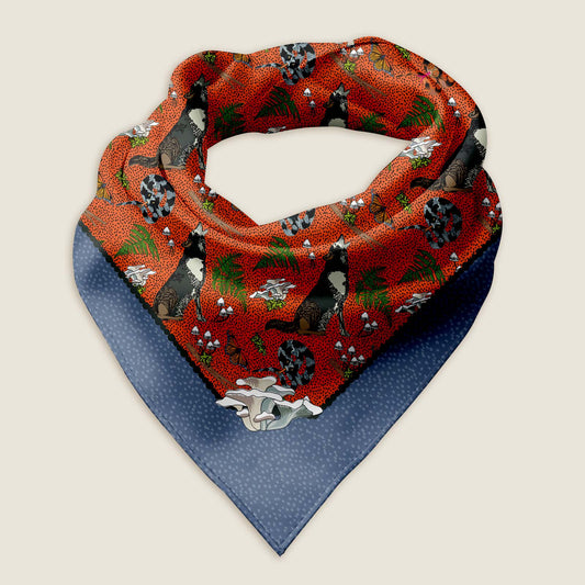 Wolf bandana scarf on an ivory background. This is an image of the Wild Wolf bandana scarf styled into a wrap showing the hand-drawn artwork of howling wolves, curly snakes, moss, mushrooms,  ferns, and butterflies on a red background with a warm purple border with a white dot pattern. 