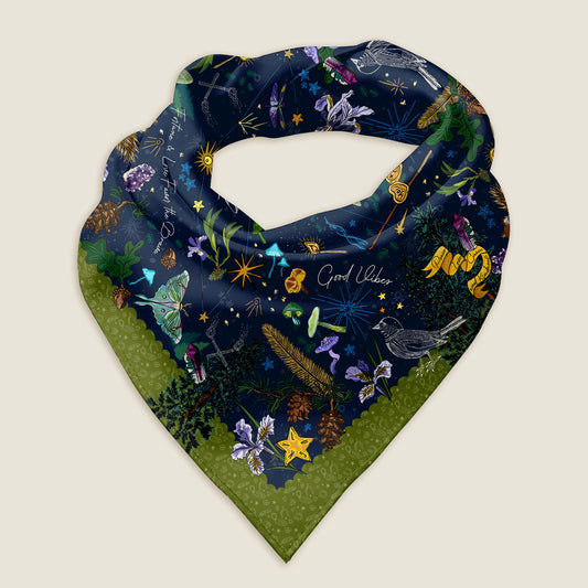 The Cygnus stars bandana on an ivory background. It shows details of the hand-drawn artwork, which includes the Cygnus constellation stars, vibrant mushrooms, luna moths, crystals, burning matches, wild iris, lucky stars, pine trees, and birds. All of these represent good fortune and blessings.  The color palette is deep blues and greens with purples and yellows.
