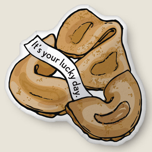 Fortune cookie-shaped pillow on an ivory background.