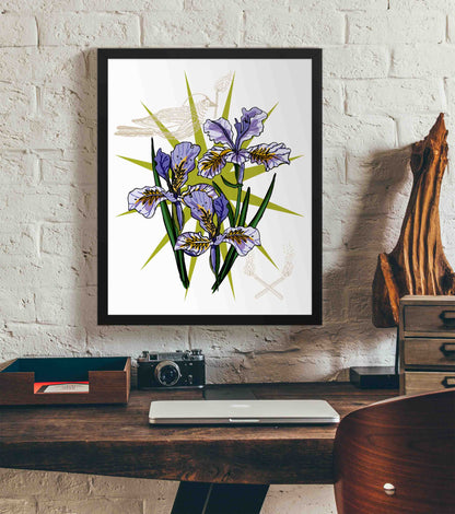 This photo shows the framed Florals, Flames, and Free Bird art print hanging on a white brick wall. Below it, there is a wood. The desk has a camera, laptop, and wood sculpture on it.