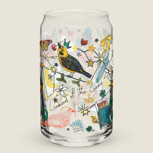 The Aquarius Constellation glass tumbler on an ivory background. The artwork on the glass is an illustration of the Aquarius Constellation, said to be the "luckiest of the lucky" stars. The illustration includes a golden finch with a crown, cherries, crescent moons, matches, bows, and other symbols of good fortune. The color palette is primarily golden yellows, deep turquoise, red and black.