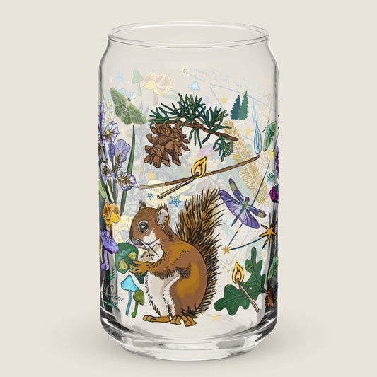 The Cygnus Constellation glass tumbler on an ivory background. The artwork on the glass is an illustration of the Cygnus Constellation, considered by sailors to be a good omen. The illustration includes a cheeky squirrel eating a green mushroom, pinecones, dragonflies, burning matches, oak leaves, acorns, iris flowers, pine tress, and other symbols of good fortune. The color palette is primarily forest greens, deep turquoise, purple and golden yellows.