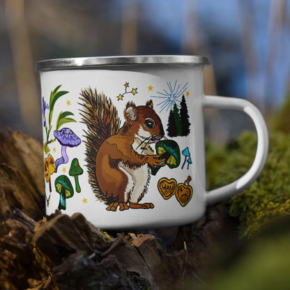 The Cyngus Stars Camp Mug sitting on a tree stump in the woods. The color of the enamel cup is white and the artwork is hand drawn illustrations of the Cygnus constellation, considered by sailors to be a good omen. The illustration includes a cheeky squirrel eating a green mushroom, pinecones, dragonflies, burning matches, oak leaves, acorns, iris flowers, pine trees, and other symbols of good fortune. The color palette is primarily forest greens, deep turquoise, purple and golden yellows.