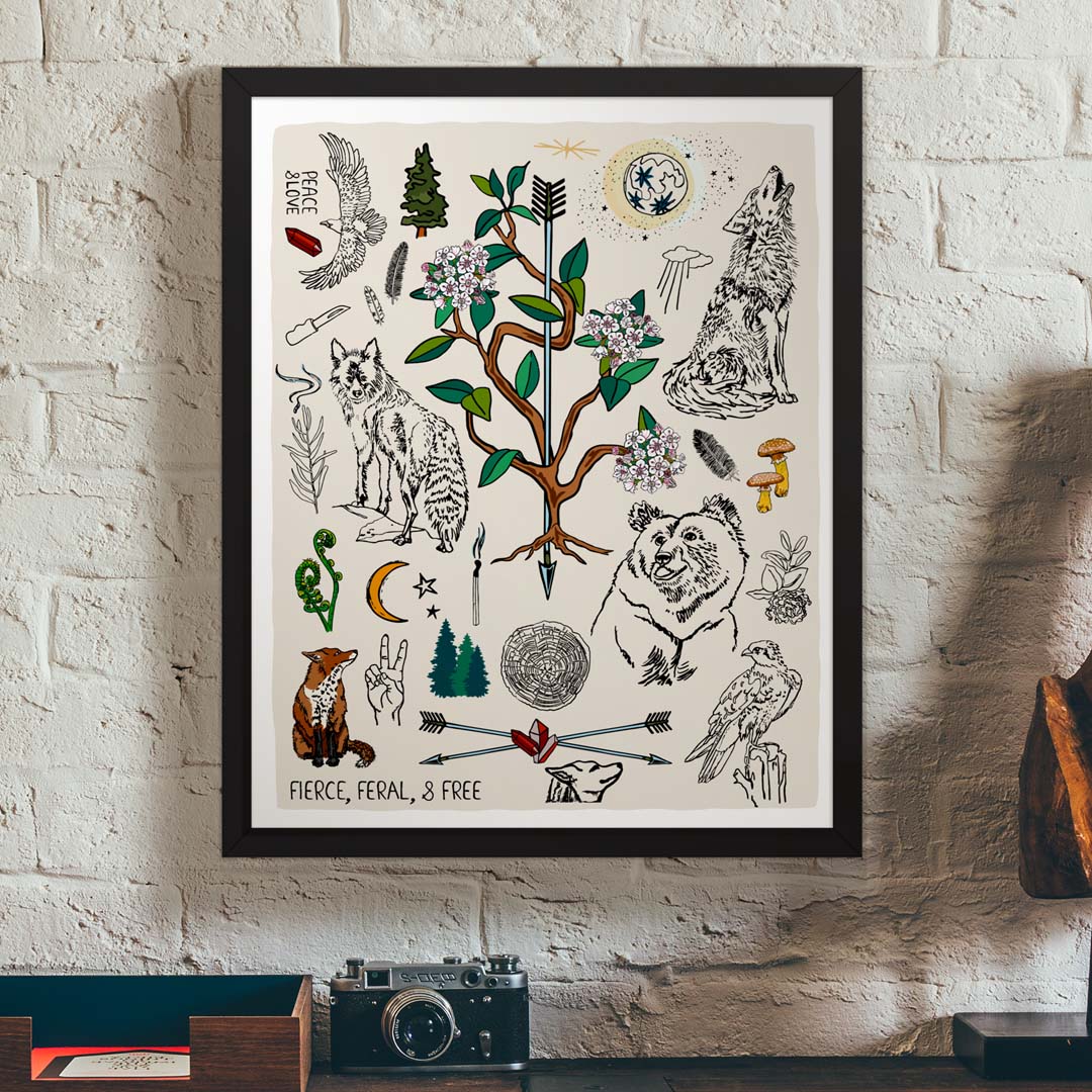 Fierce, Feral, and Free art print poster in a black wood frame hanging on a brick wall, above a vintage desk.
