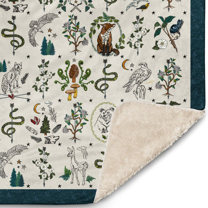 Close-up of the corner of the Fierce, Feral, and Free blanket. The illustrations include wild mushrooms, bears, eagles, foxes, crystals, crescent moons, deer, and other mystical nature symbols.
