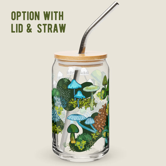 The Green Mushroom glass tumbler with the bamboo lid and metal straw option on an ivory background. The artwork on the glass is illustrations of various green and blue mushrooms, green leaves, moss, alongside pinecones and moths. The color palette is a mix of vibrant mossy greens and  earthy blues.