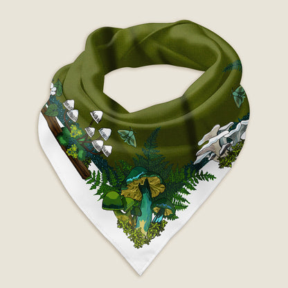 The green mushroom bandana styled as a wrap shows the details of the hand-drawn artwork, which includes a variety of green and yellow mushrooms, moths, ferns, and moss illustrated around a green middle with a white border. Behind the scarf is a green background with illustrated pine trees and the Wander Wrap logo.