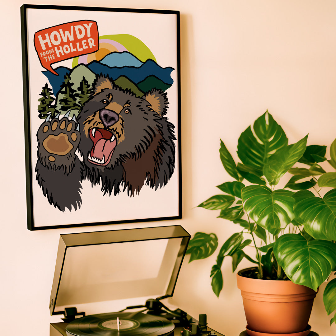 Framed bear artwork with 'Howdy from the Holler' text above a record player and plant.