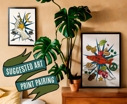 This photo shows a suggested art print pairing. This pairing shows the Lucky Charms art print in a black frame on a dresser with a plant. The companion print is the Lucky Star Giver art print, which is in a black frame on the wall.