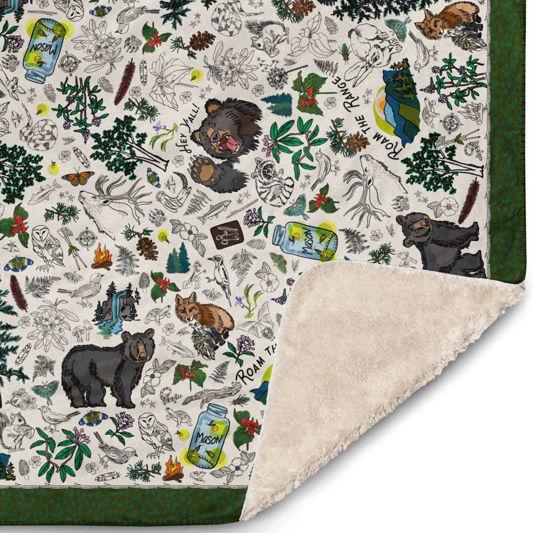 Close-up of the corner of the Mountain Adventures blanket. The illustrations include wild mushrooms, bears, pine trees, fireflies in Mason jars, snakes,  wild flowers, foxes, owls, mountain ranges, campfires, rabbits, trekking poles, and other forest icons.