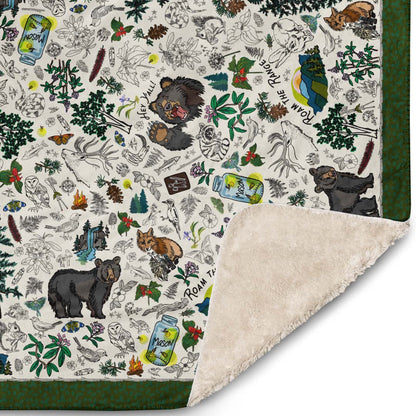 Close-up of the corner of the Mountain Adventures blanket. The illustrations include wild mushrooms, bears, pine trees, fireflies in Mason jars, snakes,  wild flowers, foxes, owls, mountain ranges, campfires, rabbits, trekking poles, and other forest icons.