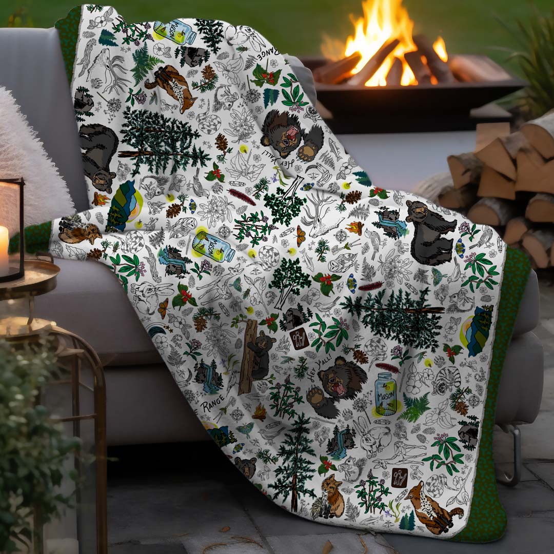 Mountain Adventures sherpa blanket draped over a couch by a fire pit in an outdoor setting.