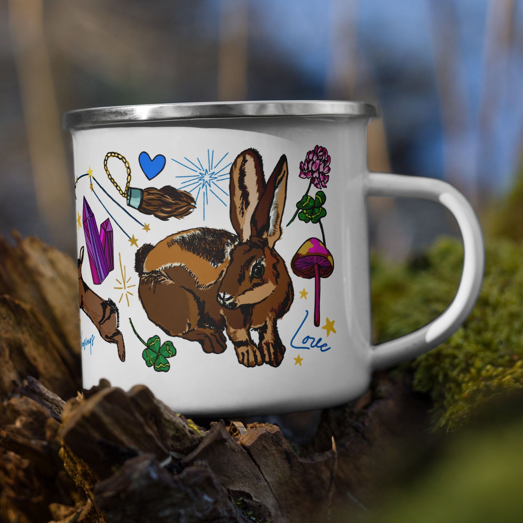 The Orion Stars Camp Mug sitting on a tree stump in the woods. The base color of the enamel cup is white and the artwork is hand drawn illustrations of the Orion constellation, which holds the "Three Lucky Stars", long considered to symbolize prosperity, longevity, and happiness. The art includes lucky rabbits, four-leaf clovers, mushrooms, stars, matches, bows and arrows for loyalty, and other symbols of good fortune. The color palette is golden yellows, pinks, forest greens, and vibrant blues.