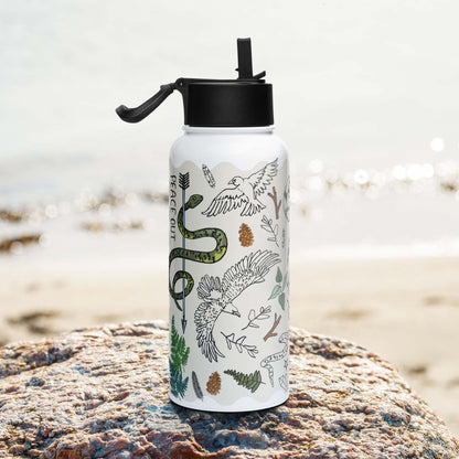 Photo showing the right side of the Peace Out in the Woods Insulated Water Bottle with Straw Lid as it sits on a rock beside  a lake.
