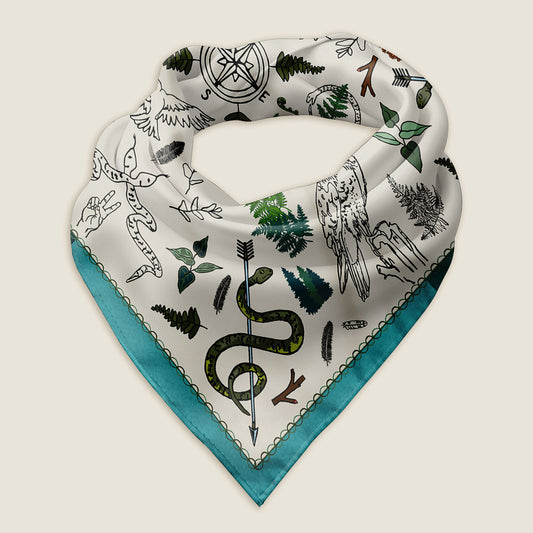 The Peace Out in the Woods bandana scarf folded into a triangle and laying on an ivory background. This view shows a close up of the hand-drawn illustration. The artwork has snakes wrapped around arrows and other poses, birds, ferns, pinecones and feathers surrounding a compass in the middle.