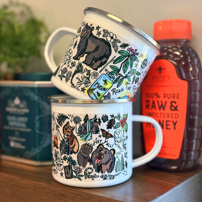 Two Mountain Hikes enamel mugs with bear and nature illustrations on a wooden kitchen shelf with a bottle of honey in the background.