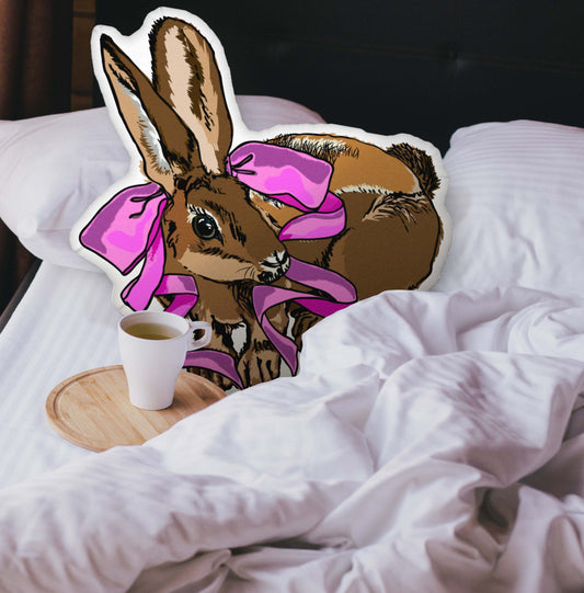 Rabbit-shaped pillow nestled in an unmade bed. There is a cup of coffee sitting on a wooden tray.