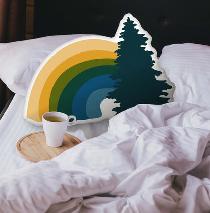 Rainbow-shaped pillow nestled in an unmade bed. There is a cup of coffee sitting on a wooden tray.