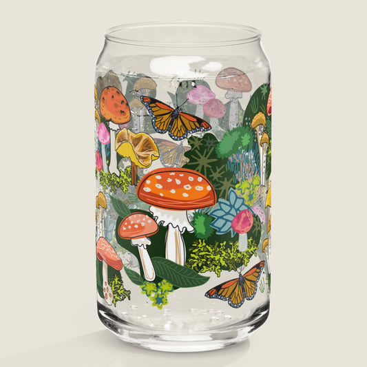 The Red Mushroom glass tumbler on an ivory background. The artwork on the glass is illustrations of various red, pink, and yellow mushrooms, green leaves, and moss, alongside yellow and red butterflies. The color palette is a mix of vibrant colors including red, pink, and yellow, with mossy greens.
