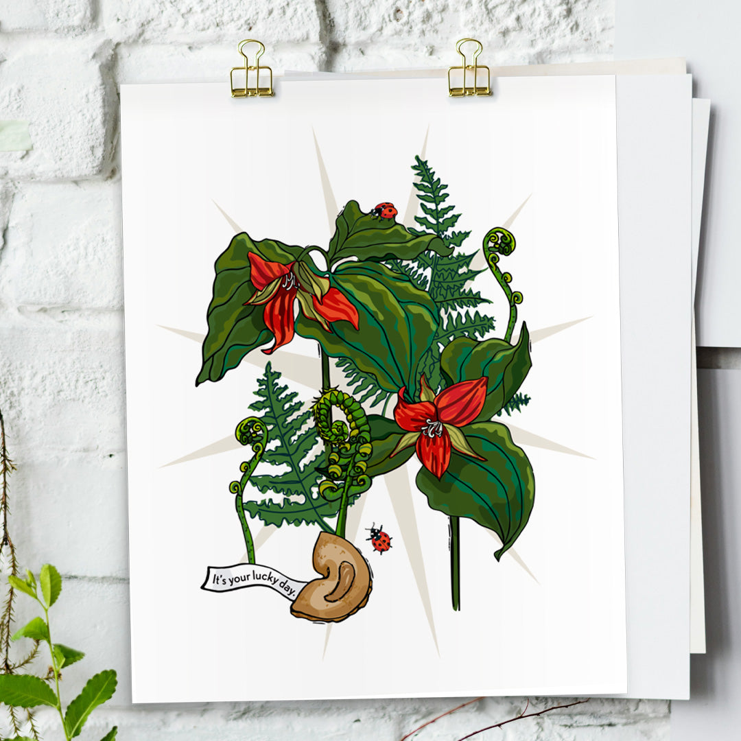 Trillium Flower art print hanging from a white bring wall with gold clips.