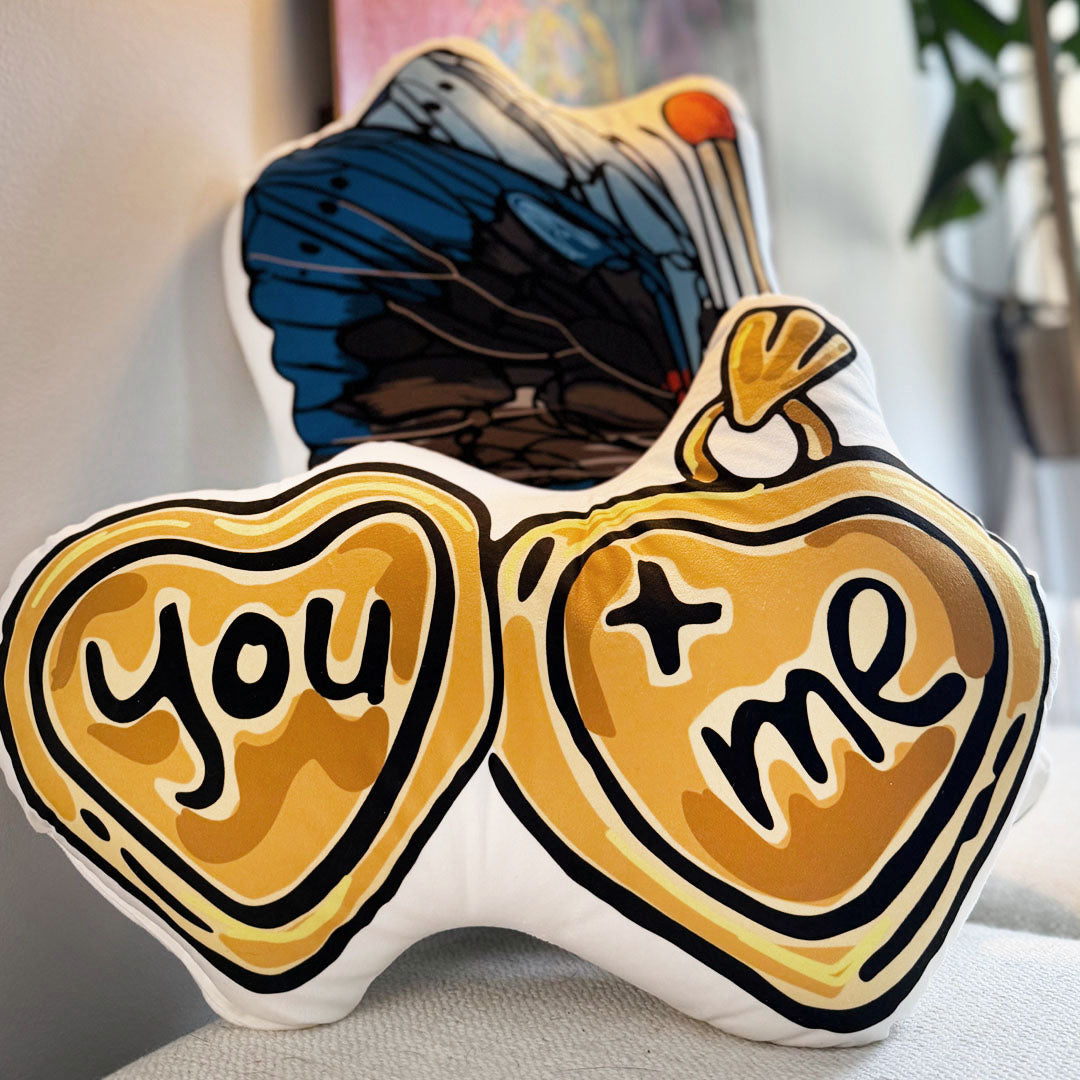The You + Me Heart-shaped Locket Pillow sitting on a fabric bench.