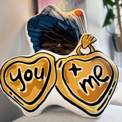 The You + Me Heart-shaped Locket Pillow sitting on a fabric bench.