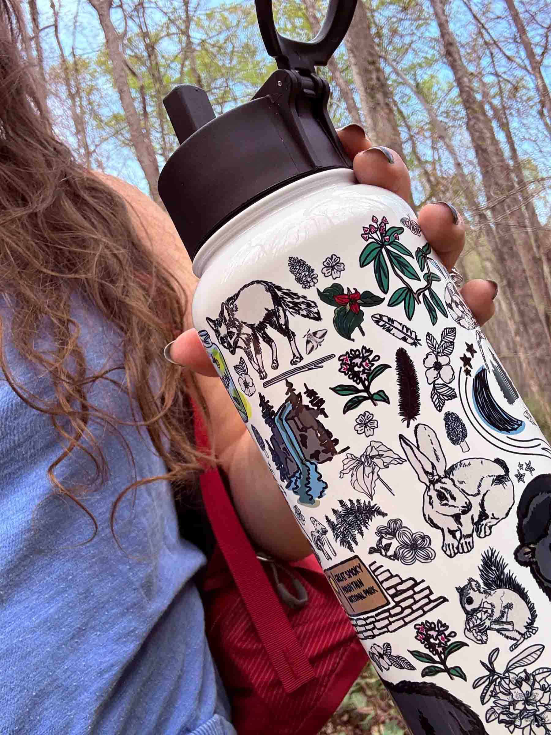 A hiker in the forest holds a close-up view of the Great Smoky Mountains insulated water bottle.