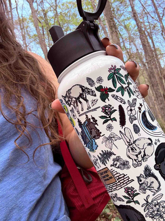 A hiker in the forest holds a close-up view of the Great Smoky Mountains insulated water bottle.