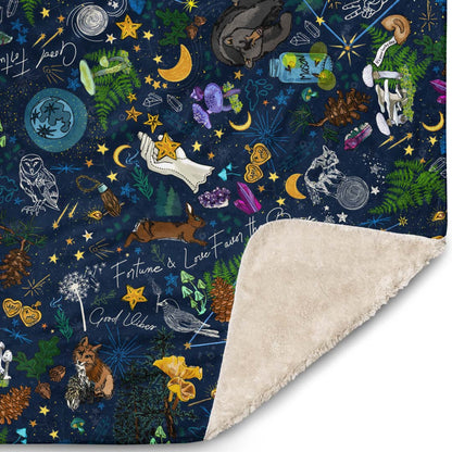 Close-up of the corner of the Under the Stars blanket. The illustrations include lucky constellations, shooting stars, wild mushrooms, ferns, rabbits, bears, foxes, crystals, crescent moons, deer, and other mystical lucky charms.