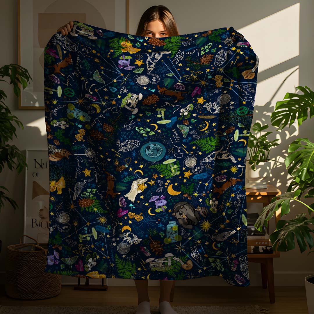 This image shows the size. It's a person holding up the Under the Stars sherpa blanket in a cozy boho-style apartment.
