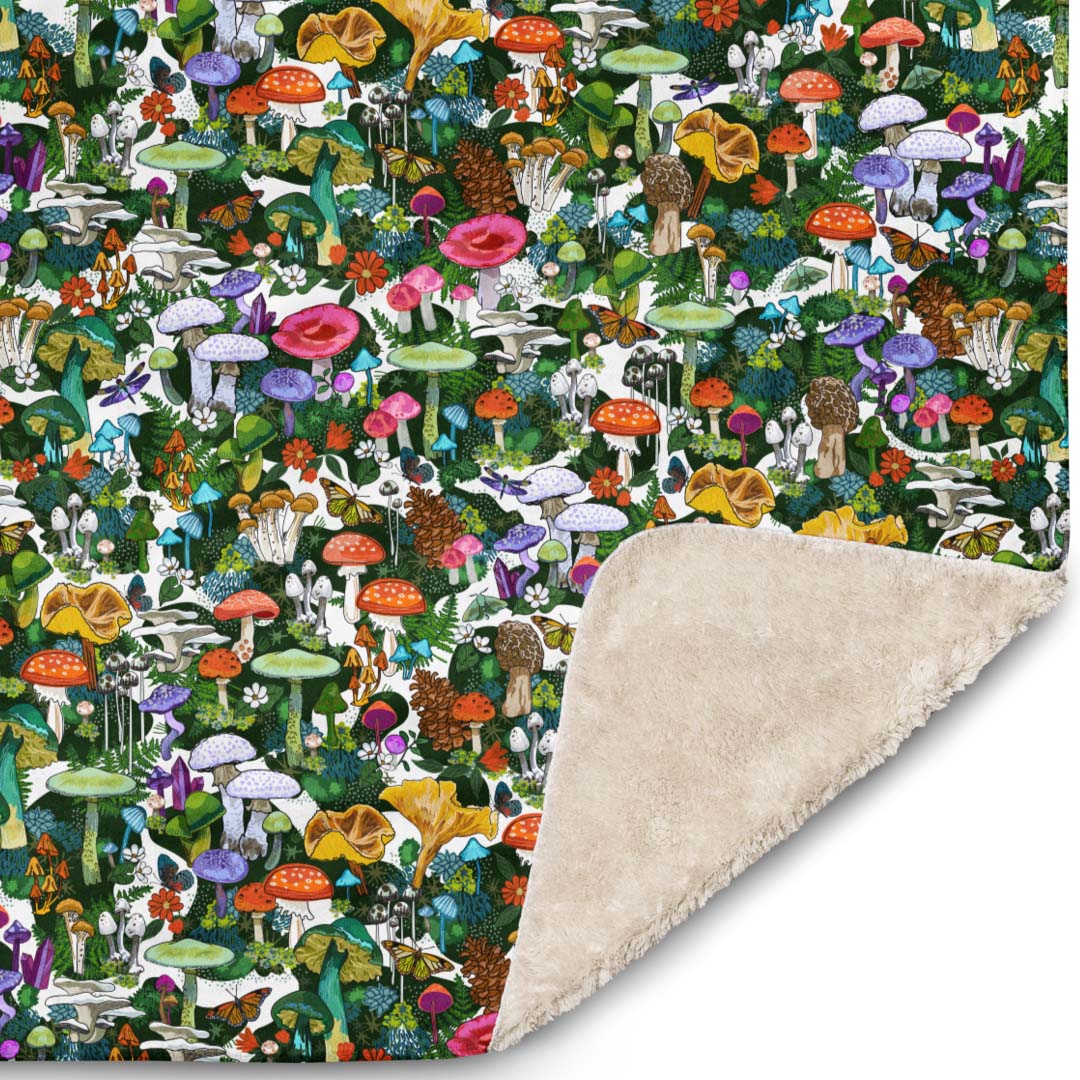 Close-up of the corner of the Wild Mushroom blanket. The illustrations include wild mushrooms of all kinds nestled in moss and the small flowers. There are also butterflies and moths in the illustration.