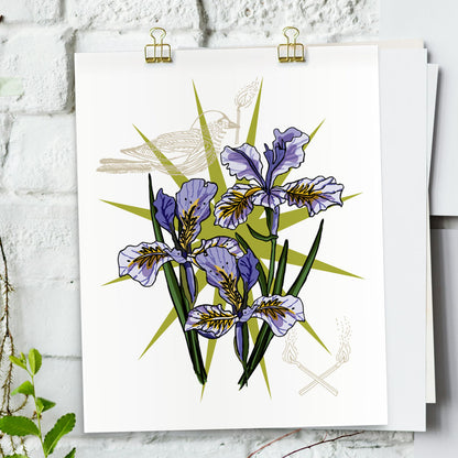 Iris and bird art print hanging from a white bring wall with gold clips.